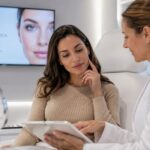 Profesional de medicina estética mostrando información en tablet a una paciente en una clínica moderna, representando email marketing y reputación de marca en salud privada.